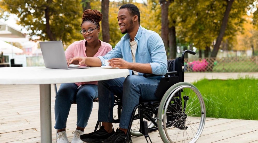 Cheerful impaired black man with female colleague using laptop together